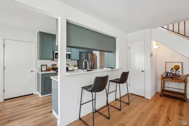 kitchen with stainless steel appliances, light wood-style floors, a breakfast bar area, green cabinets, and light countertops