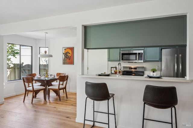 kitchen with stainless steel appliances, light wood-style floors, a peninsula, a breakfast bar area, and baseboards