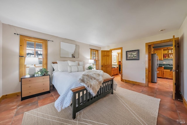 bedroom with ensuite bath, light tile patterned floors, baseboards, and freestanding refrigerator