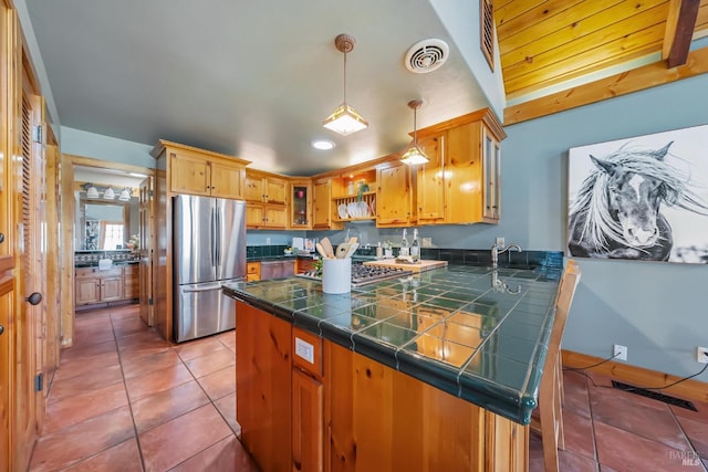 kitchen featuring tile patterned floors, visible vents, freestanding refrigerator, a peninsula, and glass insert cabinets