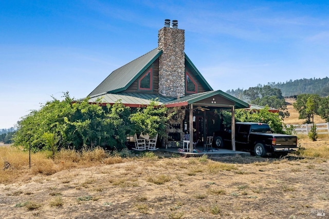 rear view of property with metal roof, a patio, a carport, and a chimney