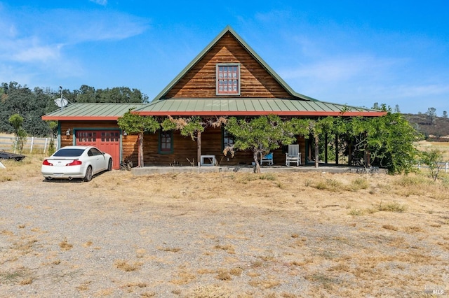 exterior space featuring gravel driveway, a porch, a standing seam roof, an attached garage, and metal roof