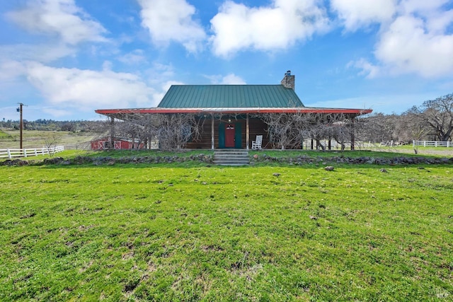 view of front of home featuring metal roof, a rural view, a chimney, and a front yard