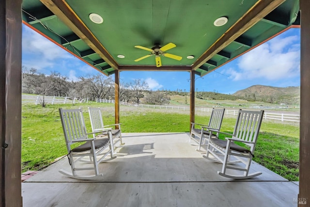 view of patio / terrace featuring a mountain view, a rural view, ceiling fan, and fence