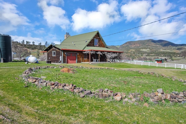 back of property featuring fence, a chimney, a garage, a lawn, and a mountain view