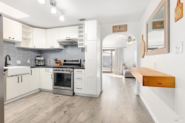 kitchen with open shelves, under cabinet range hood, a sink, arched walkways, and gas range