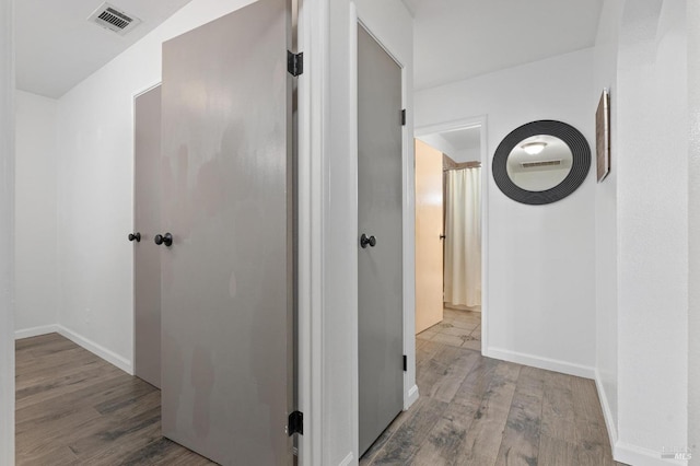 hall featuring visible vents, baseboards, and wood finished floors