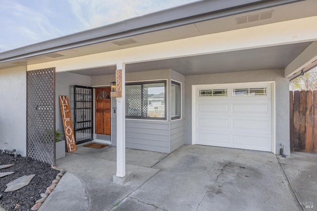 doorway to property with a garage, visible vents, driveway, and stucco siding