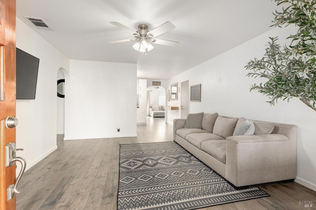 living area featuring visible vents, baseboards, ceiling fan, wood finished floors, and arched walkways