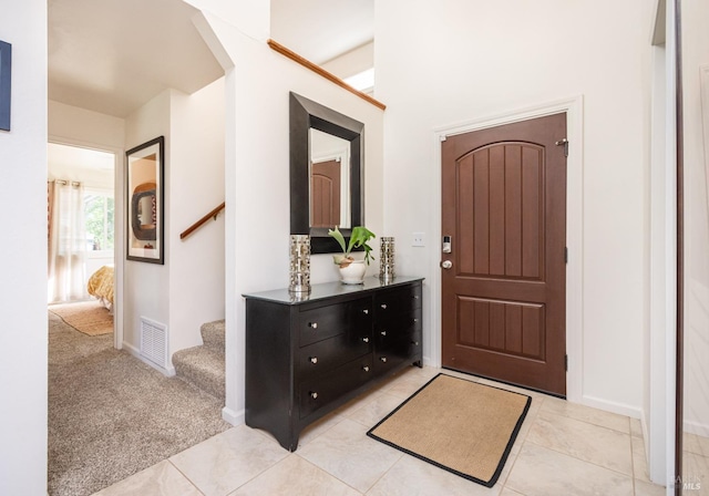 entryway featuring visible vents, baseboards, stairway, light colored carpet, and light tile patterned floors