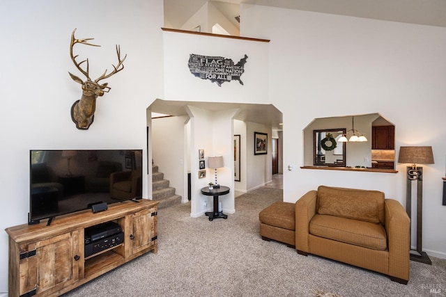 living area with baseboards, carpet, stairs, a high ceiling, and a notable chandelier