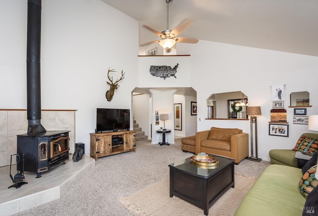 living room featuring carpet, high vaulted ceiling, a wood stove, ceiling fan, and stairs