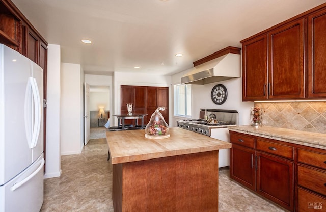 kitchen featuring tasteful backsplash, a center island, freestanding refrigerator, ventilation hood, and wooden counters