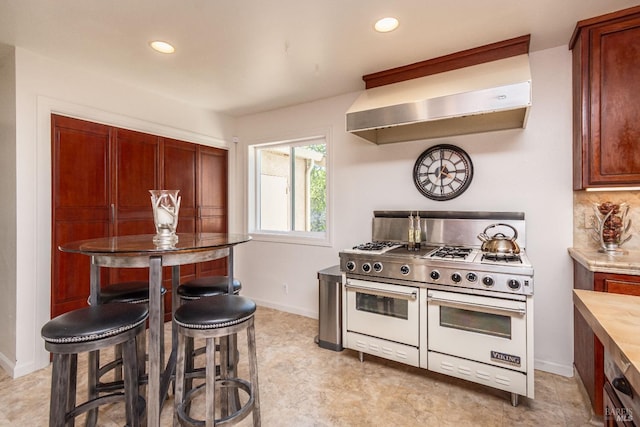 kitchen with range with two ovens, tasteful backsplash, wall chimney exhaust hood, and recessed lighting