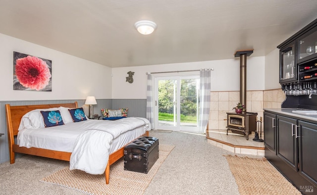 bedroom with access to exterior, a wainscoted wall, a wood stove, and a sink