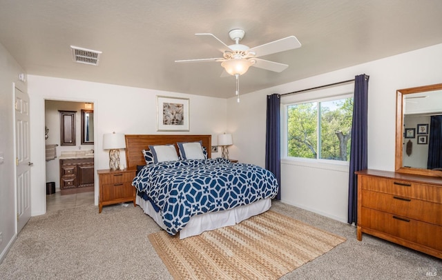 bedroom with a ceiling fan, visible vents, baseboards, ensuite bath, and light colored carpet