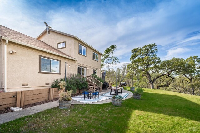 rear view of house featuring stucco siding, a yard, a shingled roof, and a patio area