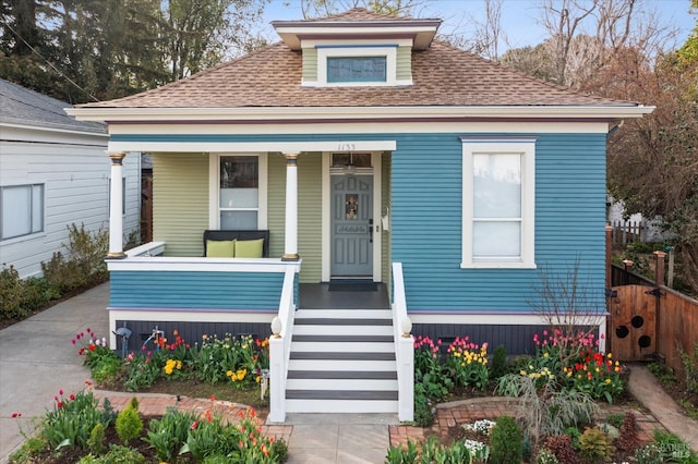 bungalow-style home with a porch, roof with shingles, and fence