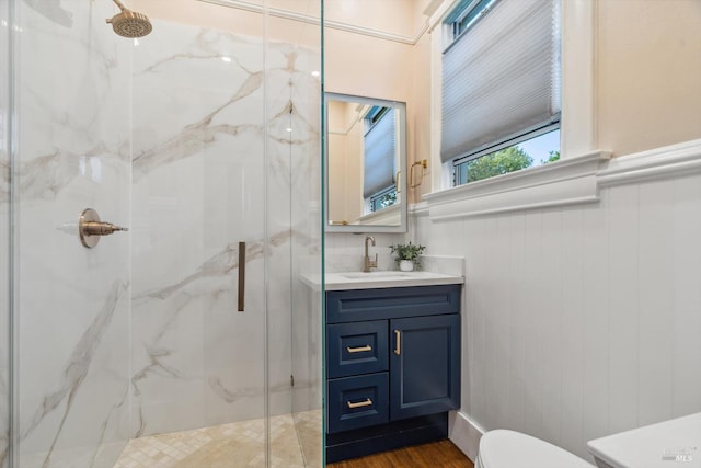 bathroom featuring a marble finish shower, a wainscoted wall, toilet, and vanity