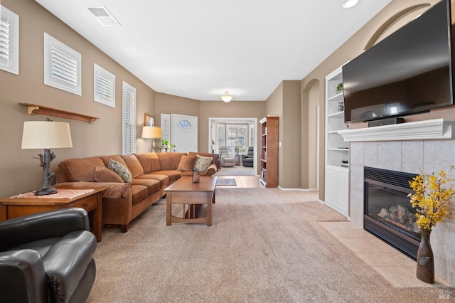 tiled living room featuring built in features, a tile fireplace, visible vents, and carpet floors