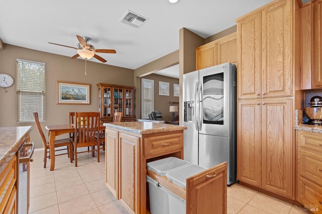 kitchen featuring light tile patterned floors, a ceiling fan, visible vents, stainless steel fridge, and a center island