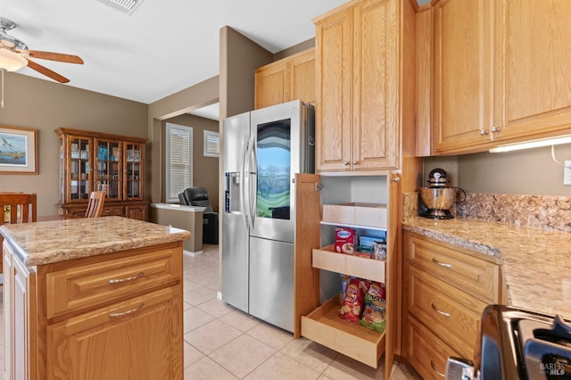 kitchen featuring a ceiling fan, light stone counters, a kitchen island, stainless steel fridge, and light tile patterned floors