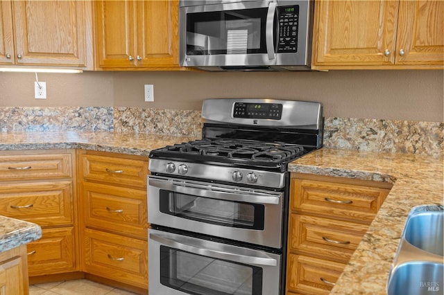 kitchen with light tile patterned floors, stainless steel appliances, and light stone counters