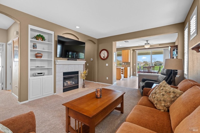 living area featuring a tiled fireplace, built in features, light colored carpet, and baseboards