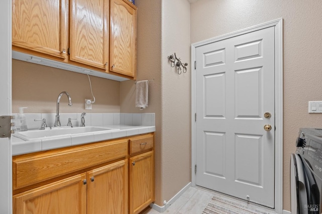 clothes washing area featuring washer / dryer, cabinet space, baseboards, and a sink