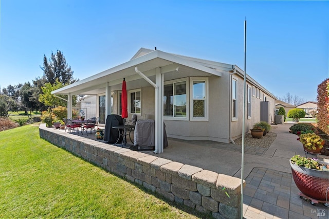 rear view of house featuring a patio area, a lawn, and stucco siding