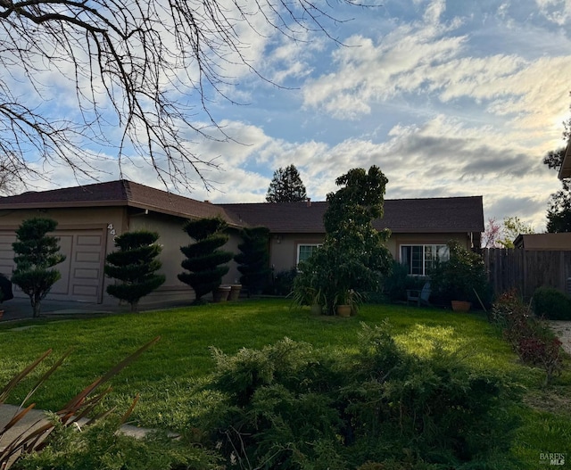 rear view of property with a garage, stucco siding, a yard, and fence