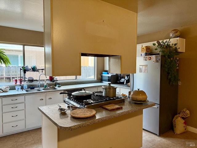 kitchen with a center island, light tile patterned floors, stainless steel appliances, white cabinetry, and a sink