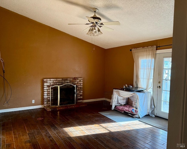 unfurnished living room featuring wood finished floors, baseboards, lofted ceiling, a textured ceiling, and a brick fireplace