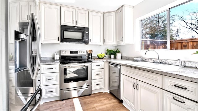 kitchen with light wood-type flooring, a sink, stainless steel appliances, white cabinets, and light stone countertops