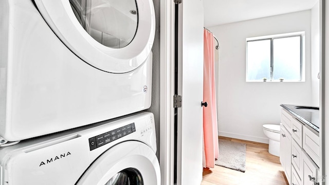 washroom featuring baseboards, stacked washer and clothes dryer, and light wood finished floors