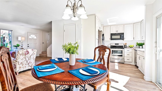 dining area with light wood finished floors, a notable chandelier, and stairway