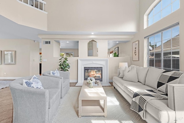 living room with visible vents, baseboards, a towering ceiling, and a glass covered fireplace