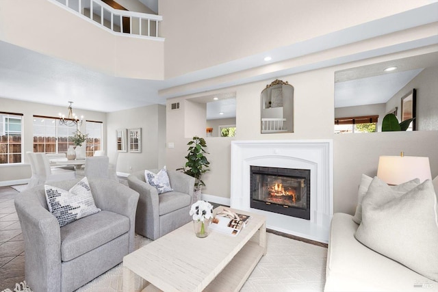 tiled living room featuring baseboards, visible vents, an inviting chandelier, a high ceiling, and a glass covered fireplace