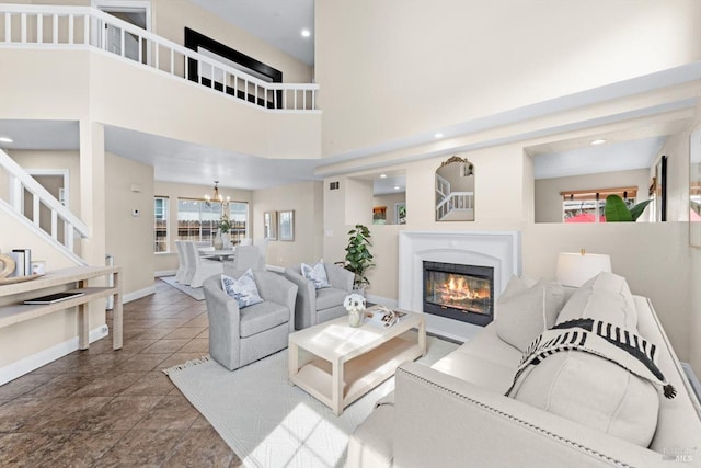 living area featuring baseboards, a glass covered fireplace, a towering ceiling, tile patterned floors, and a notable chandelier