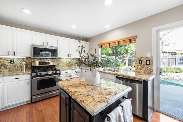 kitchen with a sink, white cabinetry, stainless steel appliances, light wood finished floors, and decorative backsplash