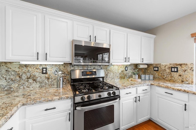 kitchen featuring light wood finished floors, backsplash, light stone countertops, white cabinets, and stainless steel appliances