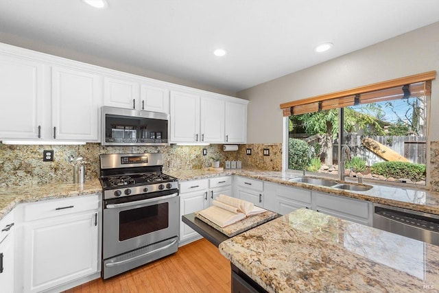 kitchen featuring a sink, white cabinetry, appliances with stainless steel finishes, light wood finished floors, and decorative backsplash