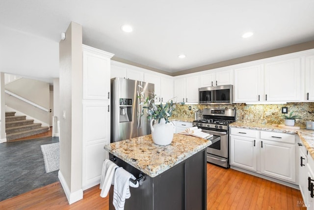 kitchen featuring tasteful backsplash, a center island, white cabinetry, stainless steel appliances, and light stone countertops