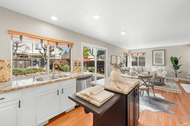 kitchen featuring a sink, light stone countertops, stainless steel dishwasher, and light wood-style flooring