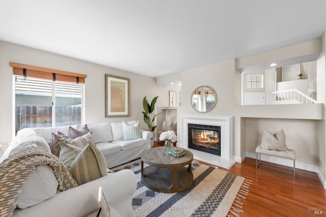 living area featuring a glass covered fireplace, wood finished floors, and baseboards