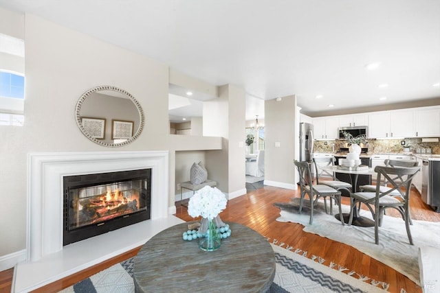 living area with a glass covered fireplace, recessed lighting, baseboards, and light wood finished floors