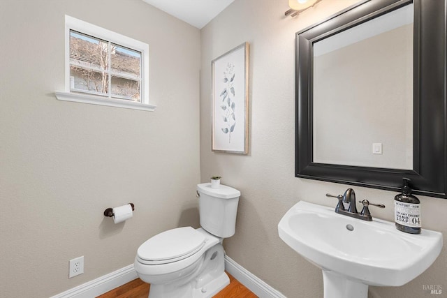 bathroom with toilet, wood finished floors, baseboards, and a sink