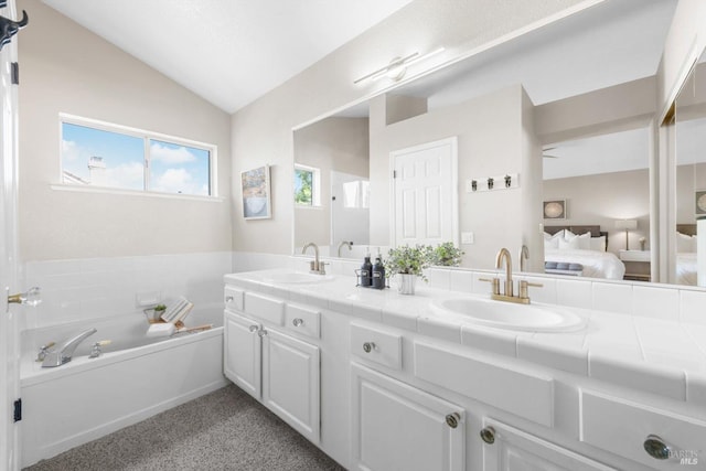 bathroom featuring ensuite bath, vaulted ceiling, double vanity, and a sink