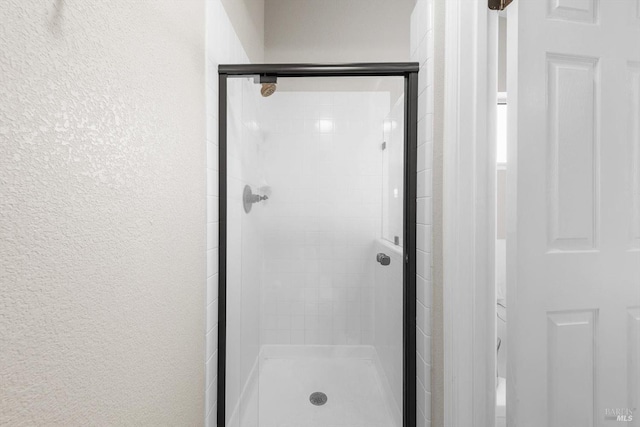 full bathroom with a shower stall and a textured wall