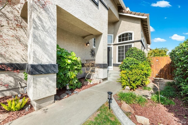 doorway to property featuring stucco siding, a tile roof, and fence